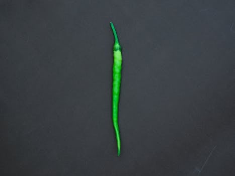Single green chili pepper centered on a dark background, showcasing a minimalist style.