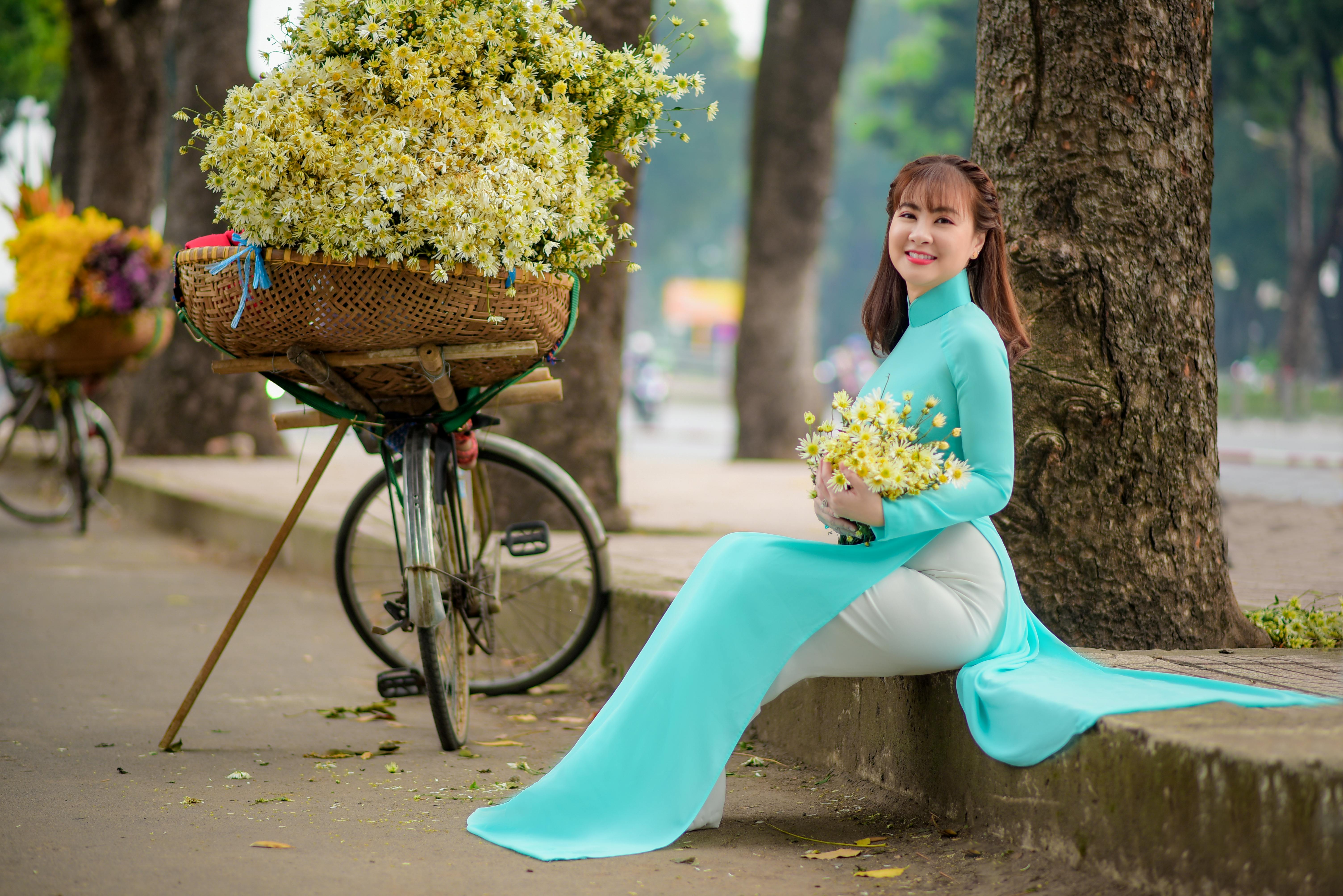 Free Woman in a Sky Blue Dress Sitting on the Roadside while Holding a Bouquet of Flowers Stock Photo