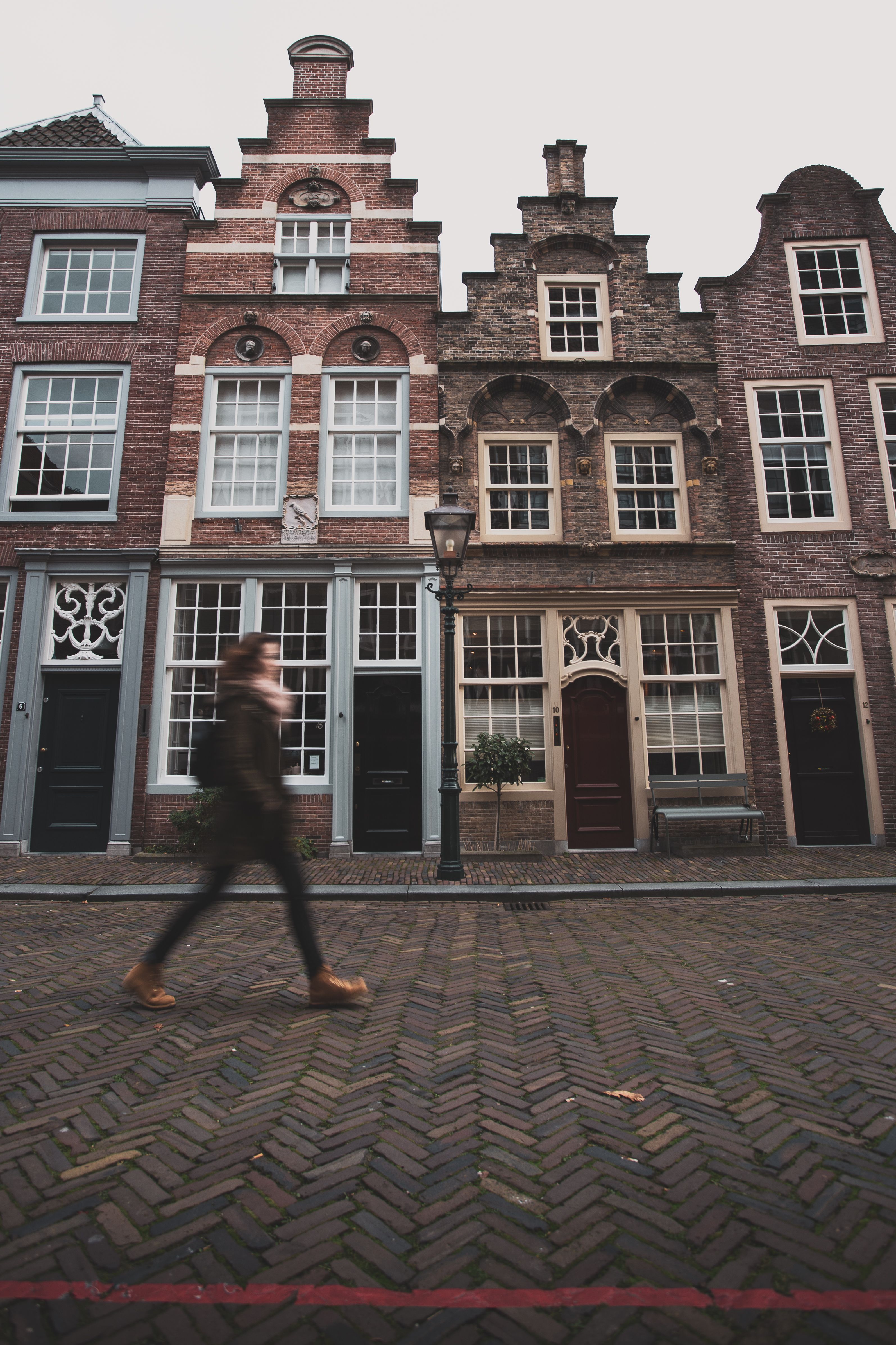 Pedestrian walking on brick-paved European street with historic gabled facades in the Netherlands