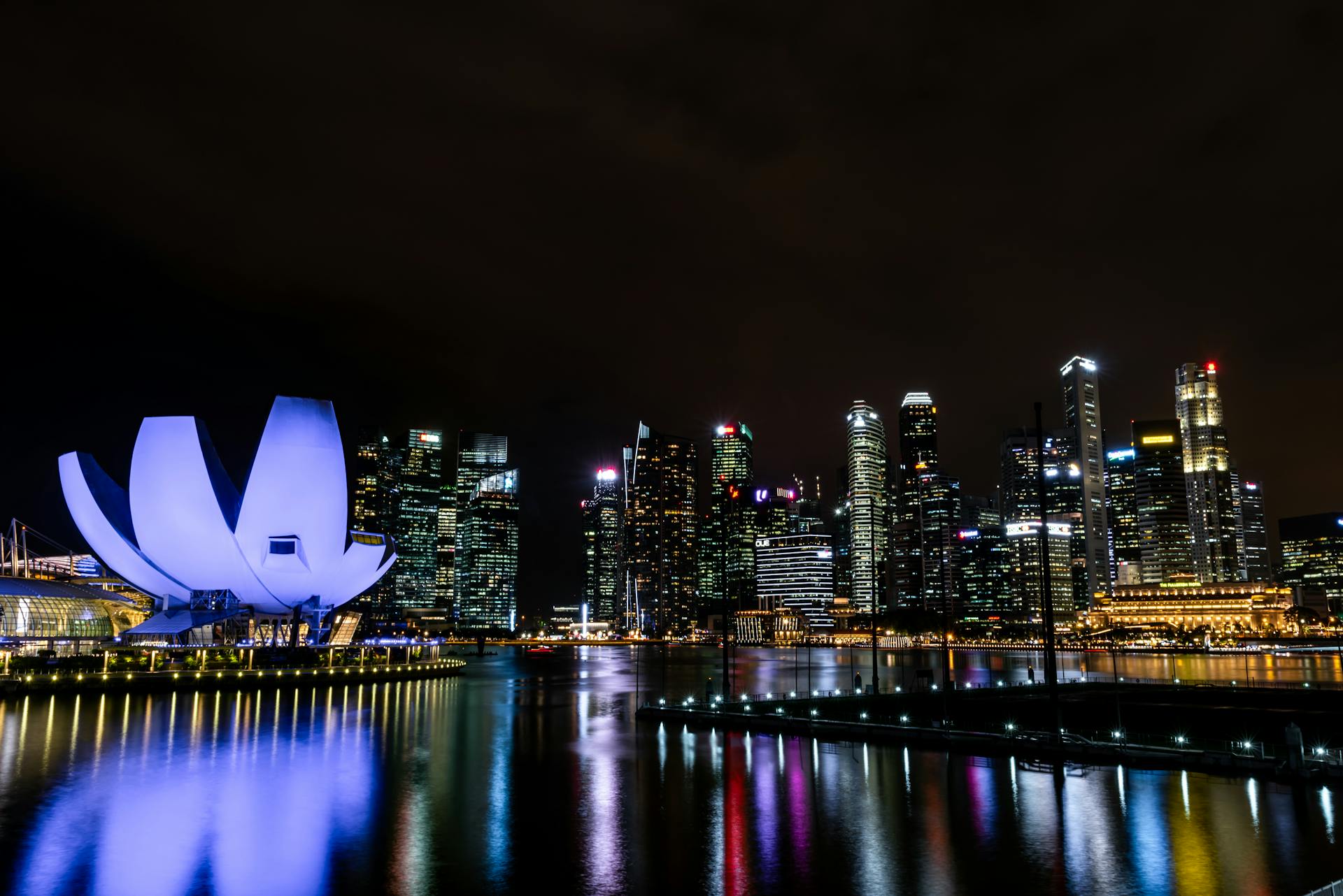 Vibrant night view of Singapore skyline with illuminated buildings and water reflections.