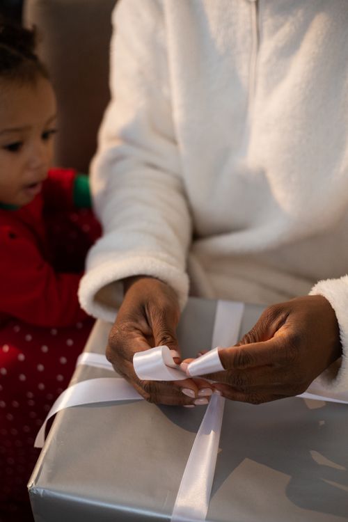 Free A woman wraps a gift while a child watches during a cozy indoor setting. Stock Photo