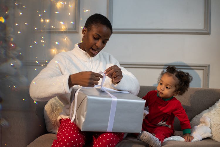 
A Woman Tying The Ribbon Of A Gift With Her Child