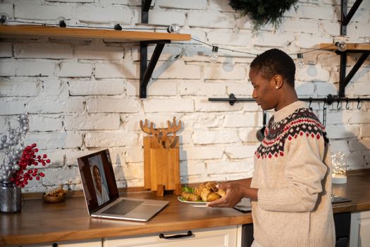 African American woman engages in a video call while holding pastries in a festive kitchen setting.