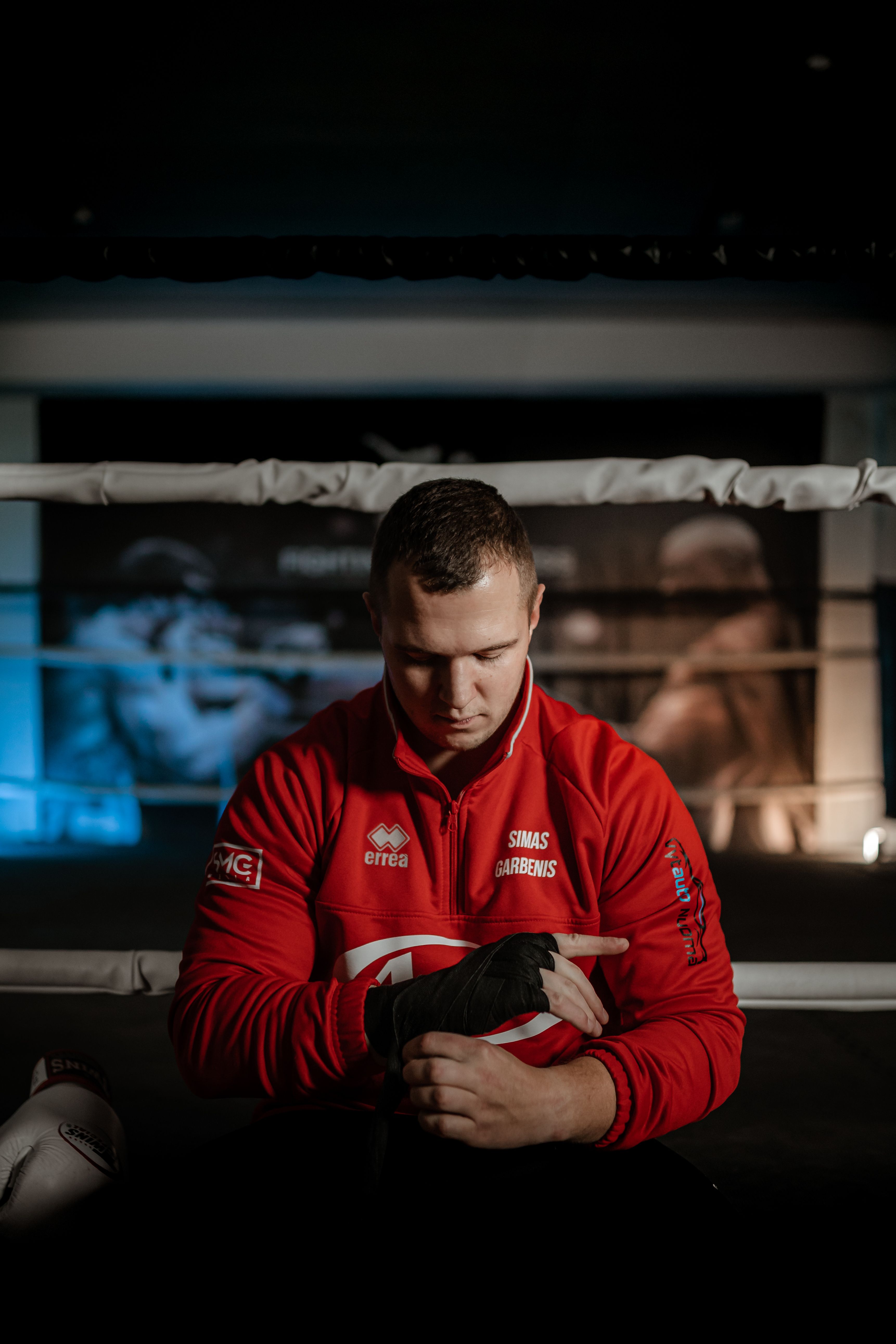 Fit sportsman in sportswear putting on hand wrap and looking down while preparing to practice boxing against ring