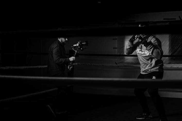 Unrecognizable Boxer And Partner With Camera During Training In Ring