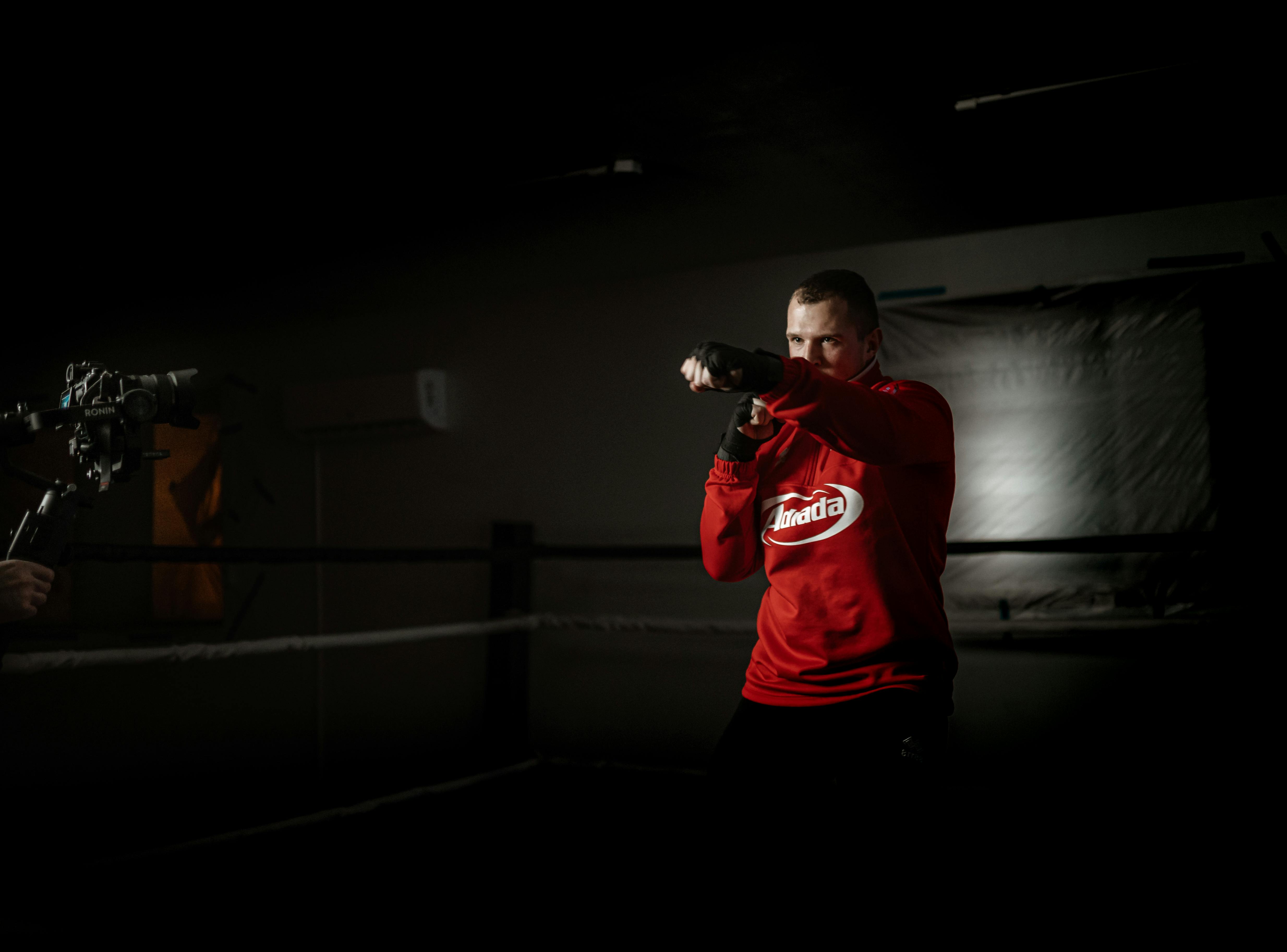 strong boxer practicing punches against crop friend with camera