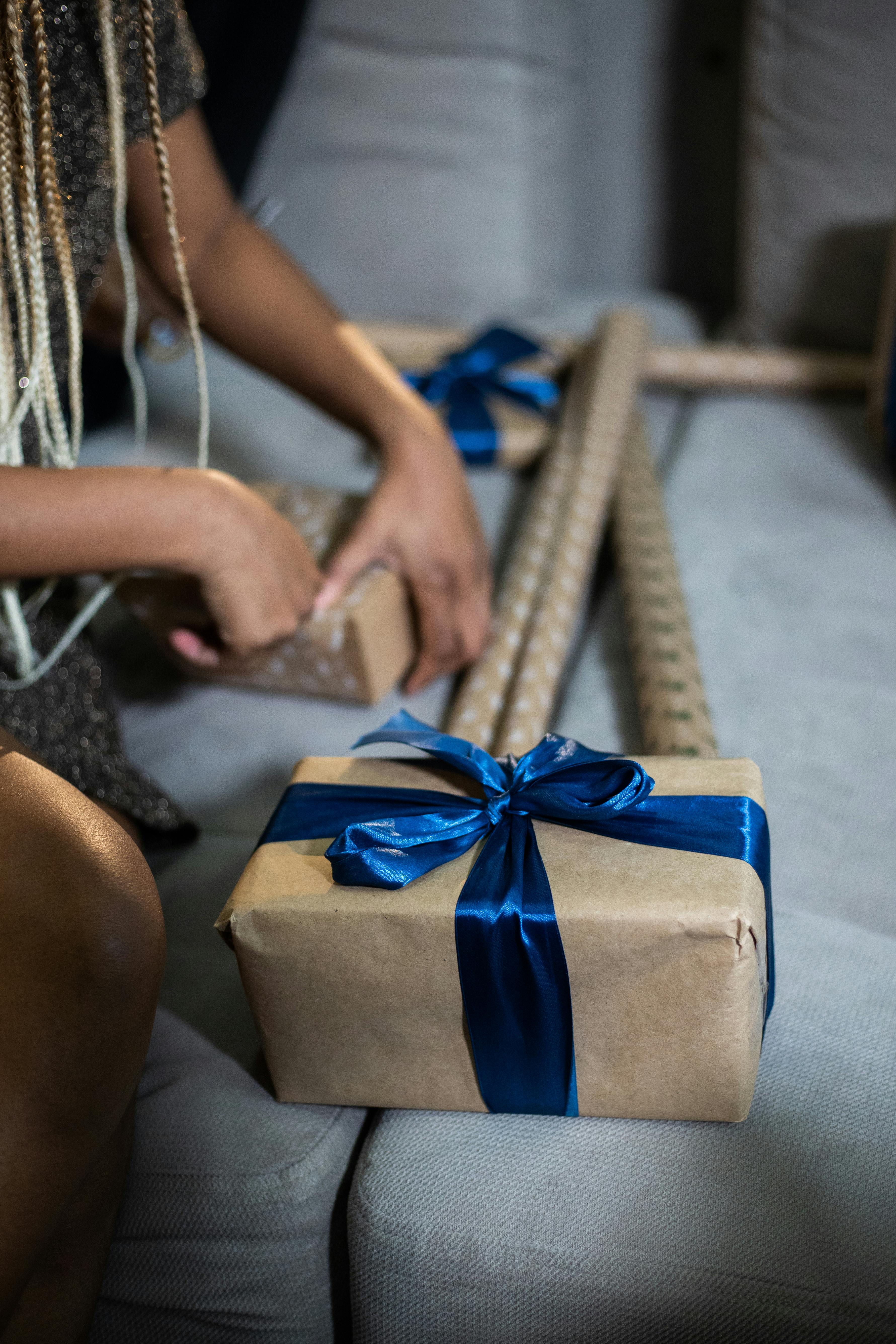 Close-up of hands wrapping Christmas gifts with blue ribbons on a couch, creating a festive atmosphere.