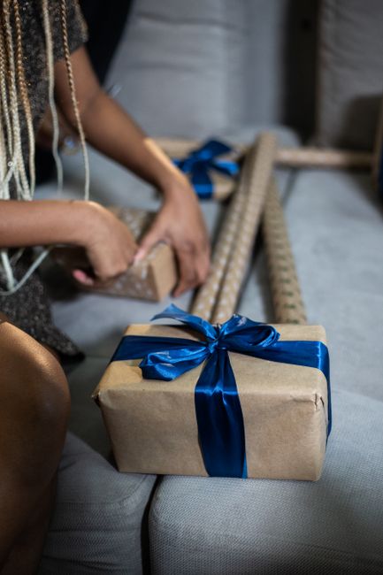 Close-up of hands wrapping Christmas gifts with blue ribbons on a couch, creating a festive atmosphere.