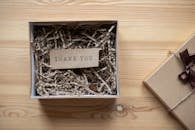 Top view of opened carton present box with small postcard with Thank You inscription and paper stuffing on wooden table