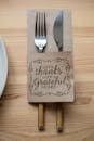 Top view of metal fork and knife in paper cover decorated with Give Thanks With A Grateful Heart inscription placed on wooden table