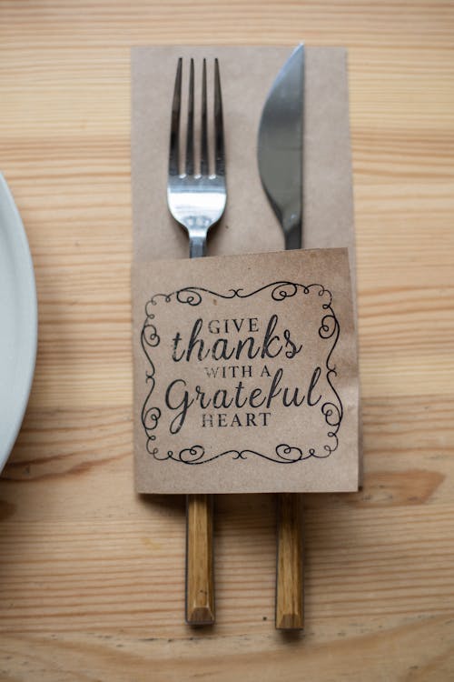 Free Top view of metal fork and knife in paper cover decorated with Give Thanks With A Grateful Heart inscription placed on wooden table Stock Photo