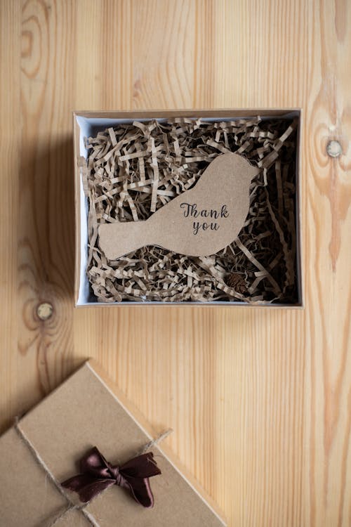 Free From above of paper postcard with Thank You inscription cutout in shape of bird and placed in open cardboard gift box on table Stock Photo