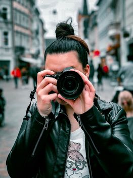Urban street scene featuring a person in a black leather jacket taking a photo.