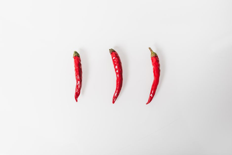 Three red chilies arranged on a white background in a minimalist style.