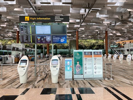 Airport customs check - Spacious airport lobby featuring flight information displays and self-check-in kiosks.