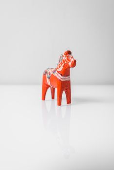 Close-up of a vibrant red Swedish Dalahorse on a reflective white background.