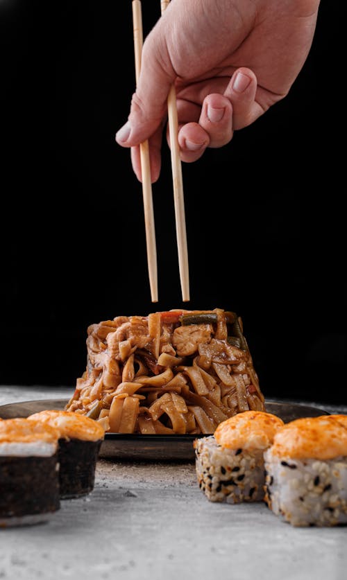 Crop faceless person with chopsticks eating Asian noodles