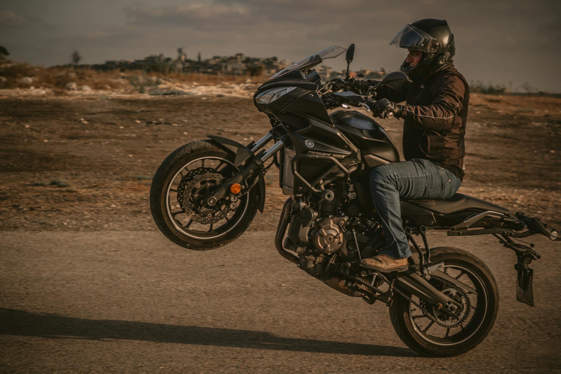 Man in helmet performing a wheelie on motorcycle on an open road, showcasing adventure and skill.