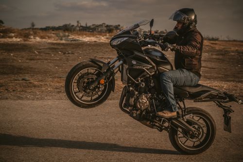 Free Man in helmet performing a wheelie on motorcycle on an open road, showcasing adventure and skill. Stock Photo