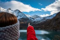 Person in Red and White Pants Near Lake and Snow Covered Mountain