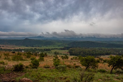 Expansive rural landscape with rolling hills under dramatic cloudy sky, conveying tranquility and remoteness.