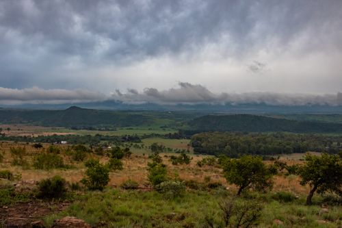 Free Expansive rural landscape with rolling hills under dramatic cloudy sky, conveying tranquility and remoteness. Stock Photo