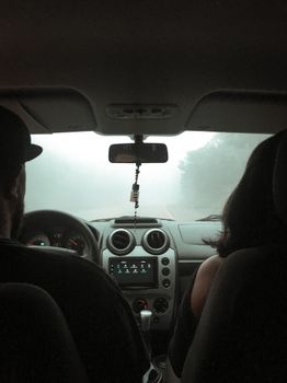 View from a car interior during a foggy drive, focusing on the dashboard and windshield with two adults.