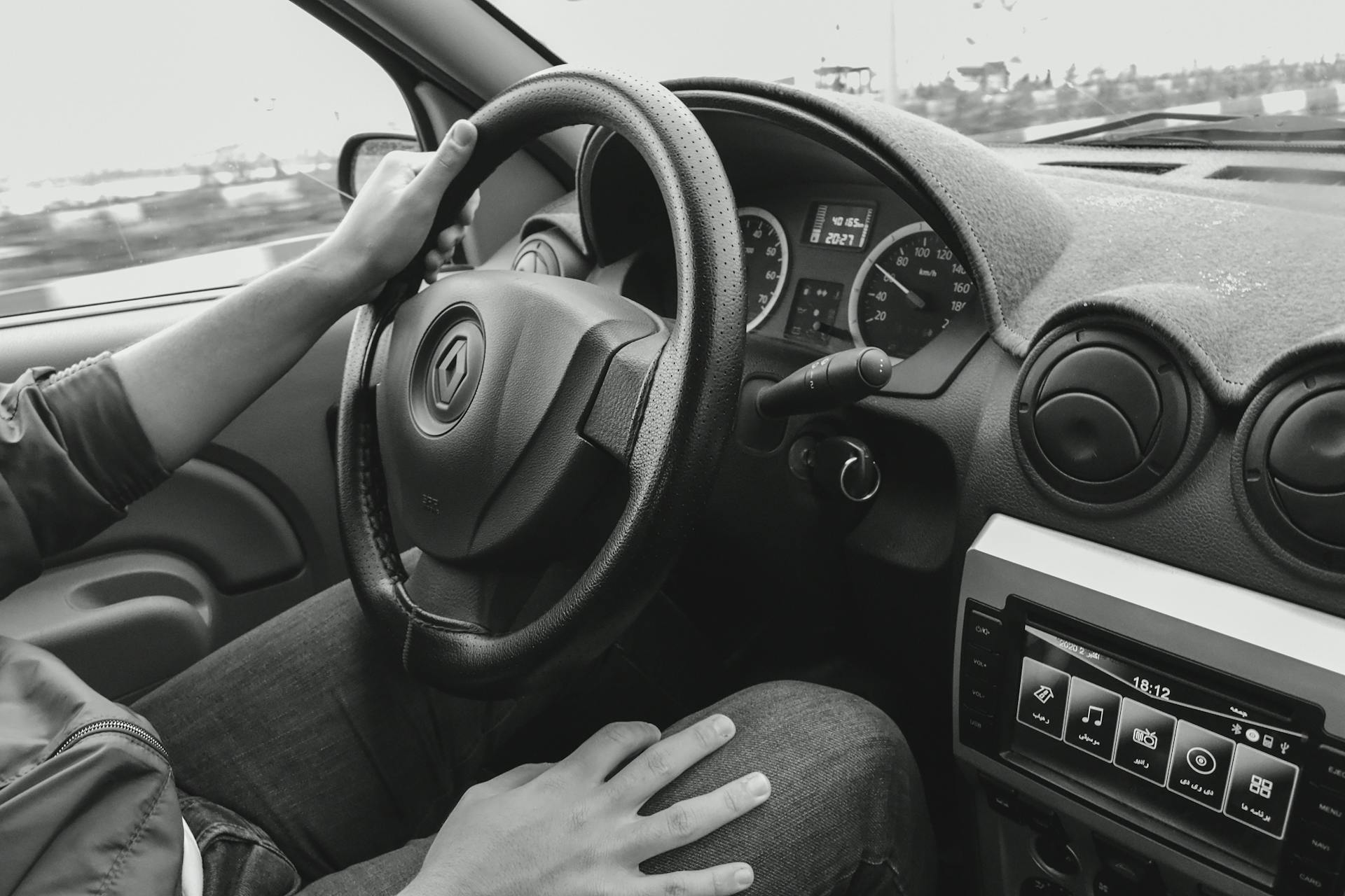 Monochrome view of a person driving a car, focusing on steering and dashboard details.