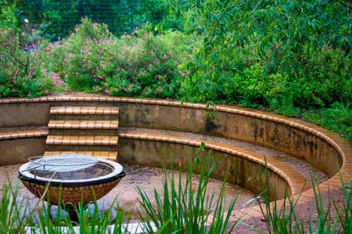 Free Peaceful circular garden with lush greenery and a central water feature surrounded by benches. Stock Photo
