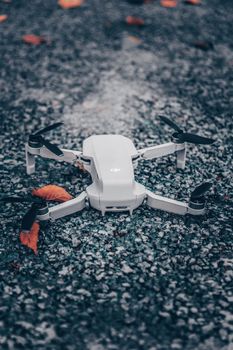 Close-up of a high-tech white drone resting on an autumn ground with scattered leaves.