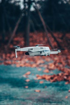 Close-up of a white drone flying outdoors over a colorful autumn background.