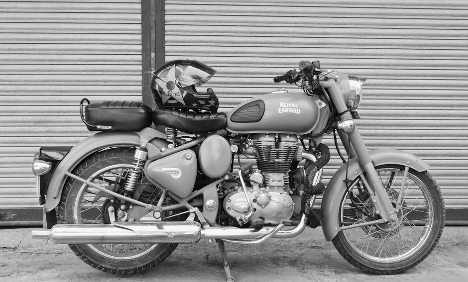 Vintage Royal Enfield motorcycle parked with helmet in grayscale, capturing its classic design.