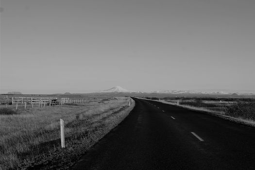 A serene black-and-white landscape photo of an empty Icelandic road stretching towards distant mountains.