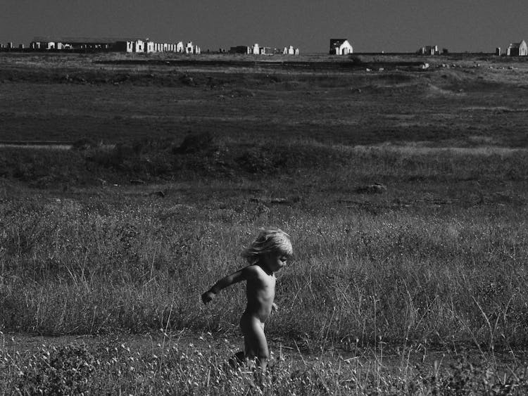 Grayscale Photo Of A Child Running Naked On Grass Field