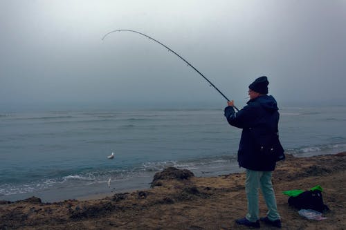 Man Standing on Seashore Catching Fish