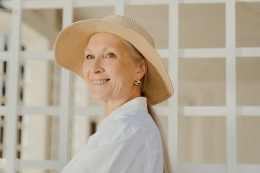 一位身着白衬衫、头戴优雅遮阳帽的女士在户外微笑着，散发着温暖的气息