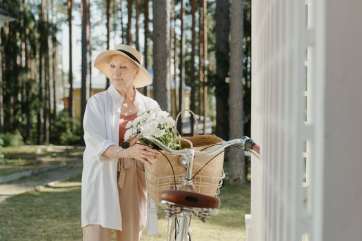 阳光明媚的日子里，一位时尚的老年妇女把自行车和鲜花放在户外的篮子里