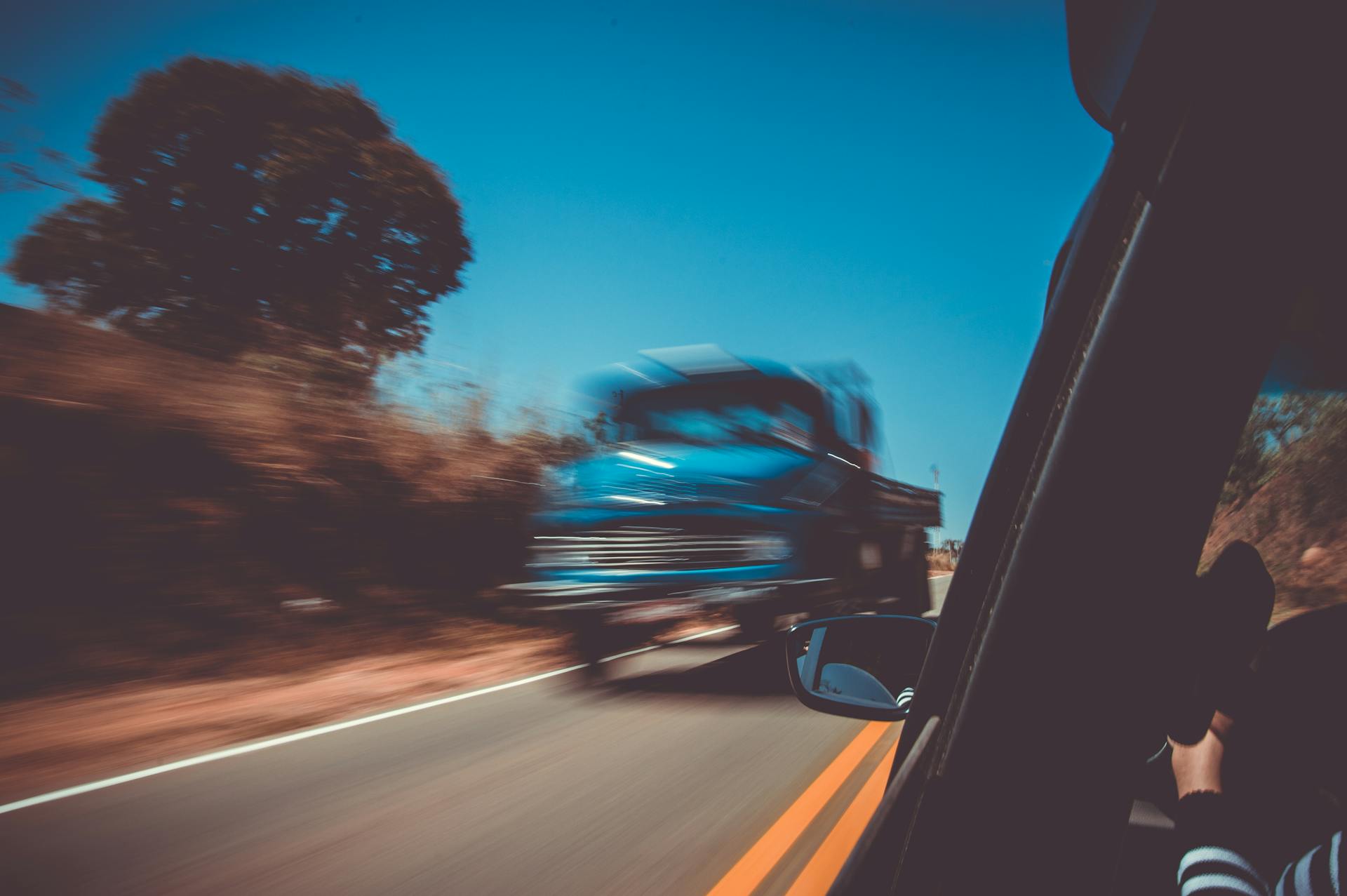 Blurred motion of a blue truck speeding on a sunny highway, captured from a car window.
