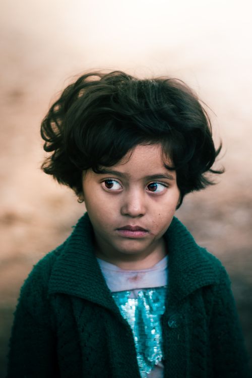 Free Portrait of a young girl in a green sweater looking contemplative in an outdoor setting. Stock Photo