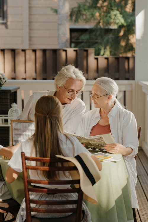 Free Elderly couple sitting together outside, sharing a tender moment on a veranda with family. Stock Photo