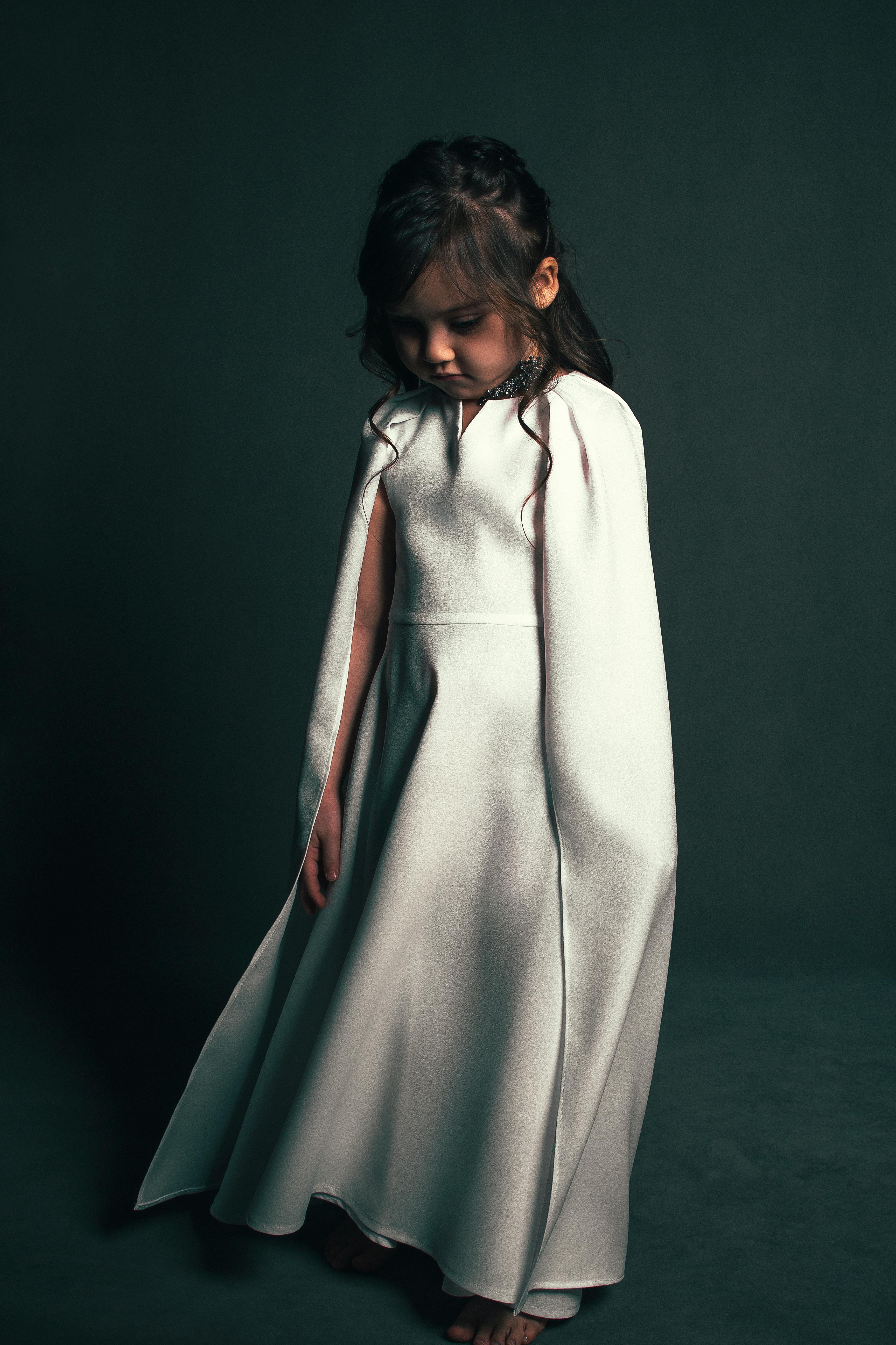 fashionable girl dressed in elegant dress with cape looking down