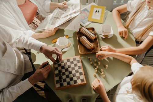 Free A family enjoys chess, tea, and pastries at a sunlit table, symbolizing togetherness. Stock Photo