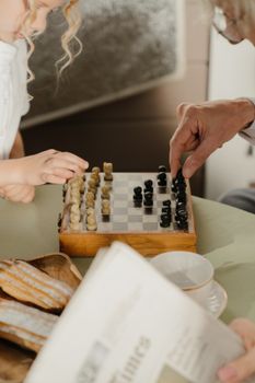 孩子在室内的木板上和老人下棋，旁边放着糕点