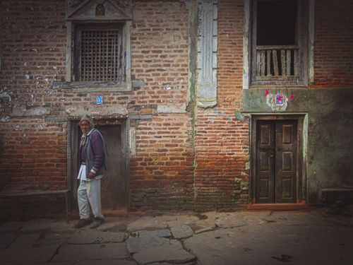 Free Side view of bearded senior ethnic male looking at camera on rough walkway near old brick building in town Stock Photo