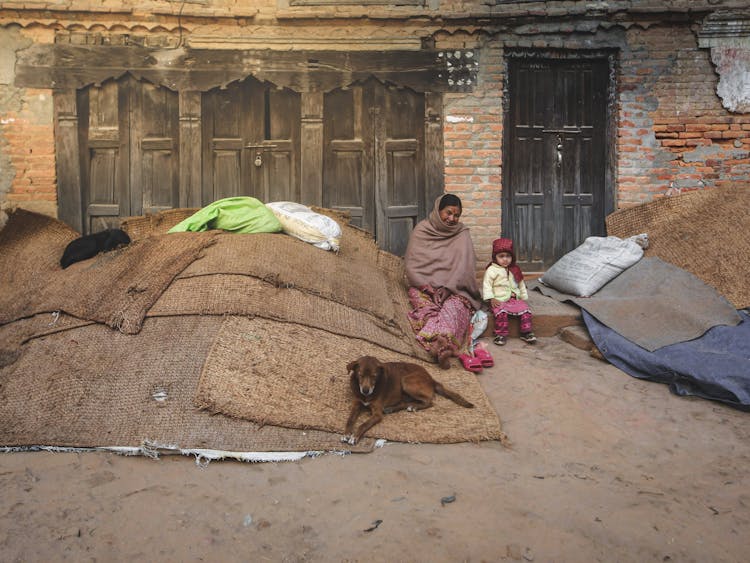 Indian Mother With Girl Near Pile Of Carpets And Dog