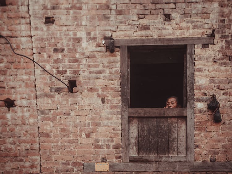 Ethnic Person Looking Out Of Old Brick House