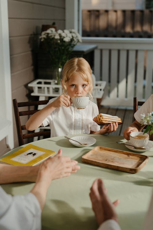 茶色の木製テーブルで食べる白いシャツの女の子