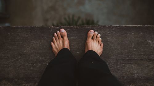 Free Close-up of bare feet standing on the edge of a wooden plank, conveying balance and introspection. Stock Photo