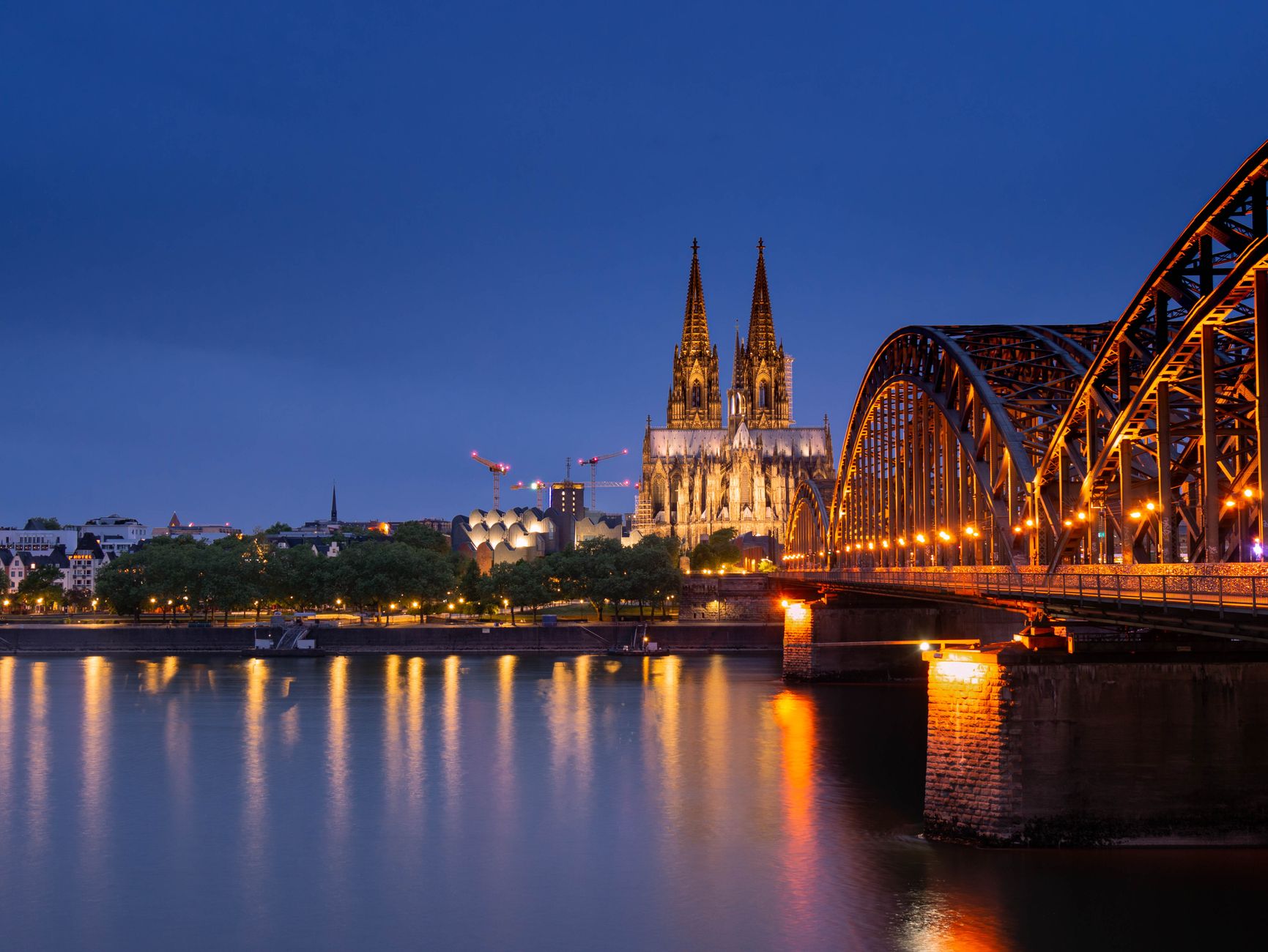 The iconic Cologne Cathedral and Hohenzollern Bridge beautifully lit up against the night sky, refle