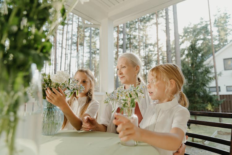 An Elderly Woman Sitting Between Two Girls Arranging Flowers